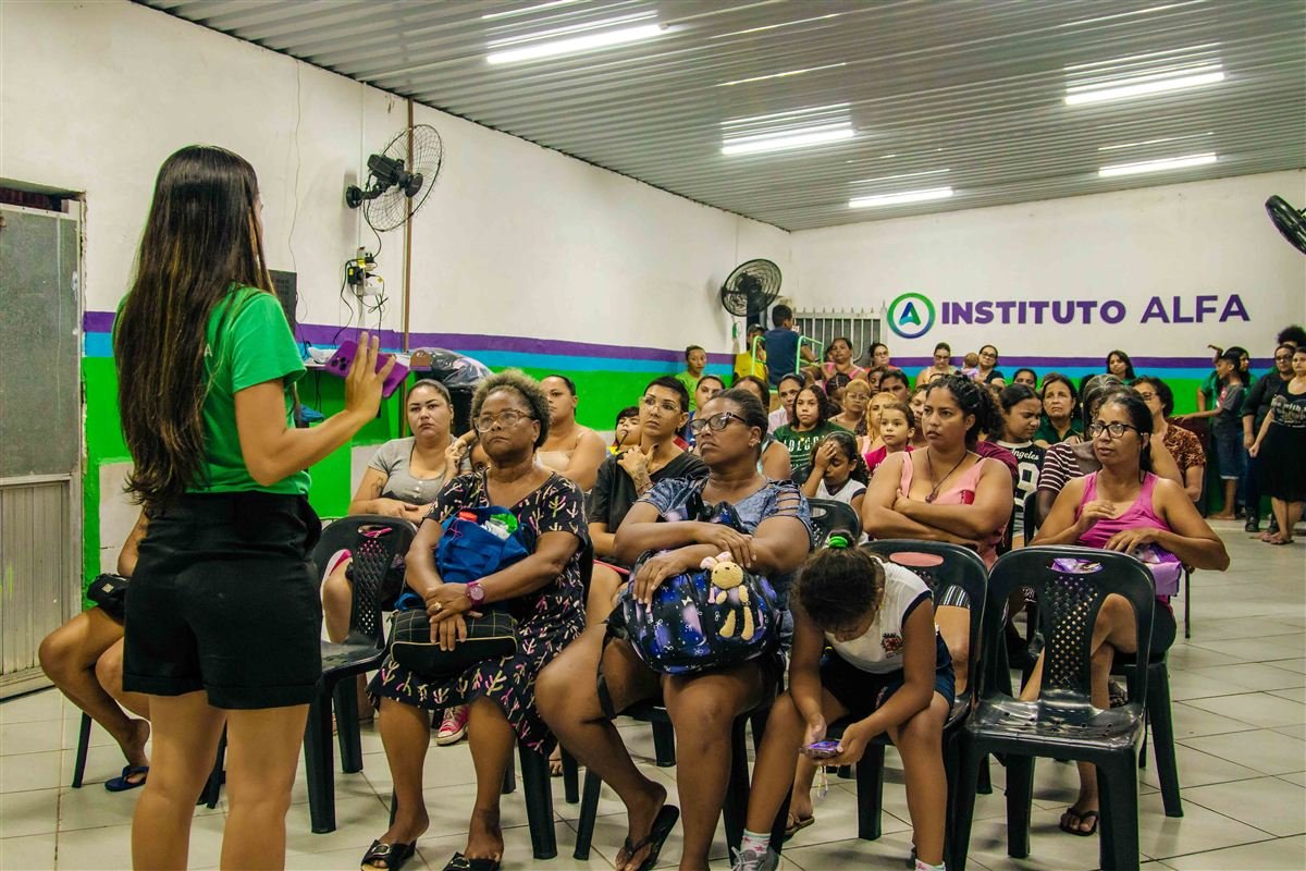 Assembleia Geral da Associação Alfa e Ômega reunindo associados e a diretoria no salão principal, com o letreiro Instituto Alfa na parede.